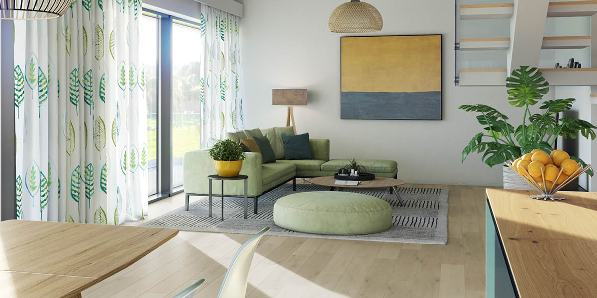 Wohnzimmer mit hellem Holzboden, grüner Couch und großem Sitzkissen. Weiße luftige Gardinen mit großen grünen Blattmustern hängen passend dazu am Fenster.